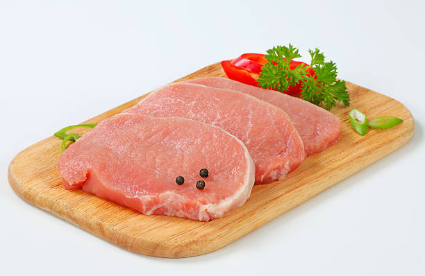 raw pork loin chops with spices on a cutting board three raw boneless pork loin chops with parsley, pepper, onion and chili peppers on a wooden cuttinga board pork stock pictures, royalty-free photos & images
