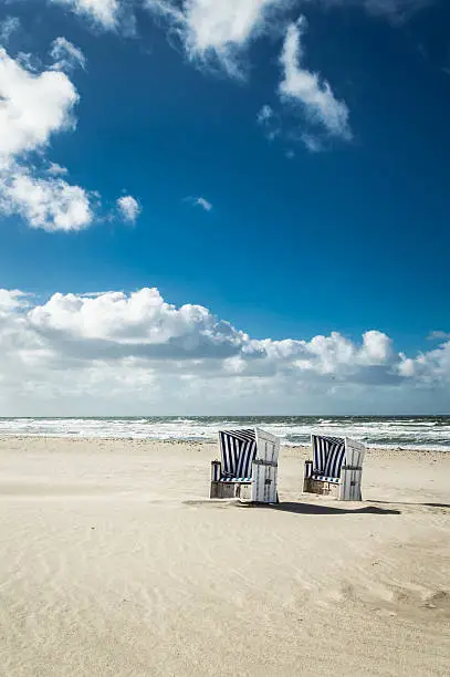 Empty hooded beach chairs at the the coastline of the island Sylt - Germany. Copy space on the blue sky in the background.