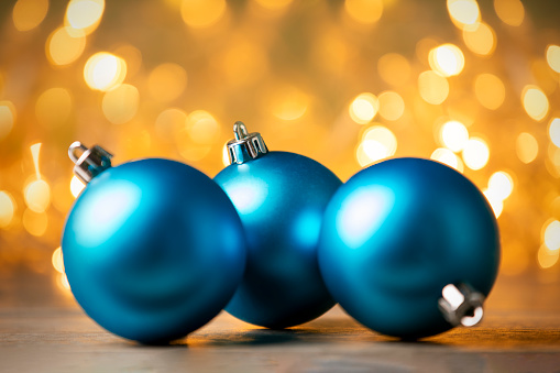 Three light blue Christmas ornaments with lights in the background.