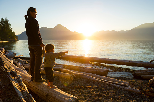Mother and daughter sharing a deep connection in a pristine natural environment that inspires friendship, aspirations and connectivity during a shared moment at sunset on the coast with mountains in the background. Experiencing nature is a great way for families to bond and make lasting memories.