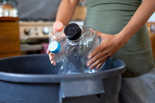 Hispanic woman putting plastic recyclables into bin