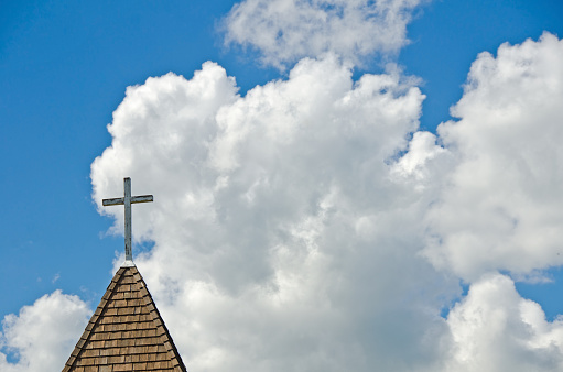 An old wood church steeple and cross with blue sky and summer clouds. Copy space.