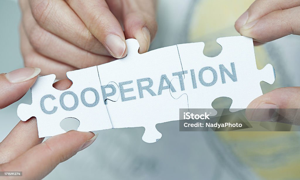 Jigsaw Puzzle - Cooperation Hands holding pieces of jigsaw puzzle with a word COOPERATION written on them. Abstract Stock Photo