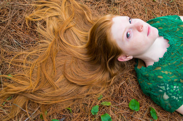 Beautiful girl wearing lace dress, spreading her long red hair on a carpet of pine needles.
