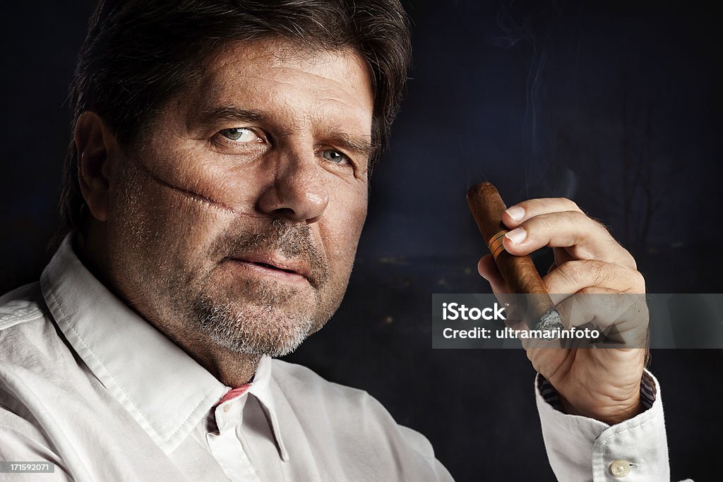 Mafia boss Close up portrait of a man with the scar on his face, holding cuban cigar. Cold and dangerous expression, deep look into camera. Gangster Stock Photo