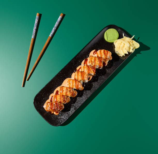 vista superior del rollo de sushi con salmón chamuscado, unagi y salsas picantes en platos negros. se muestra sobre un fondo verde intenso con sombras duras - 16490 fotografías e imágenes de stock