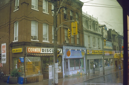 Toronto, Ontario, Canada, 1979. Row of houses with shops on a rainy day in Toronto. Also: pedestrians.