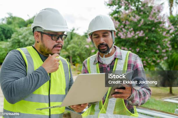 Asian Male Engineers And Architects Wear Reflective Clothing Wear A Safety Hat Check Construction Drawings From Laptop And Tapelet In Hand Discuss The Progress Of The House Construction Stock Photo - Download Image Now