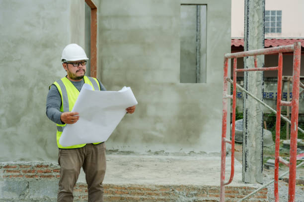 istock Asian male engineer wearing reflective vest, safety helmet, in construction zone for work safety, man walked out house under construction, spread out translation paper looked at it, when was finished. 1715966922