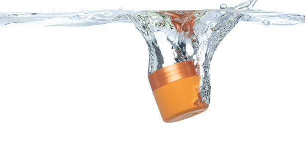 Orange Cosmetic container fall into clear water with air bubble. Cosmetic treatment container drop to clear water of freshness. White background isolated freeze element