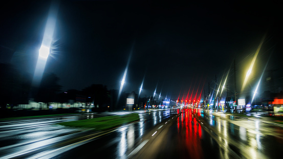 Illuminated road and defocused light trails at night. Driving on wet night road in small town surroundings. Torrential rain after storm edge in Tampa, Florida