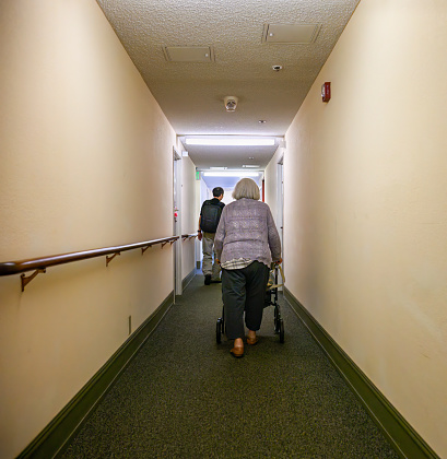 Senior woman walking using a mobility walker in the apartment corridor. Vertical format.