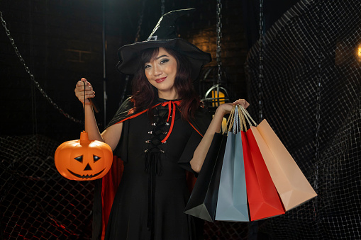 Asian girl in her witch costume holding jack'o lantern for halloween party trick or treat concept with dark black background