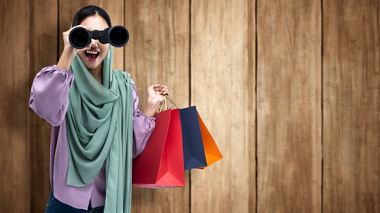 Muslim woman in a headscarf holding a binocular and shopping bags. Cyber Monday concept