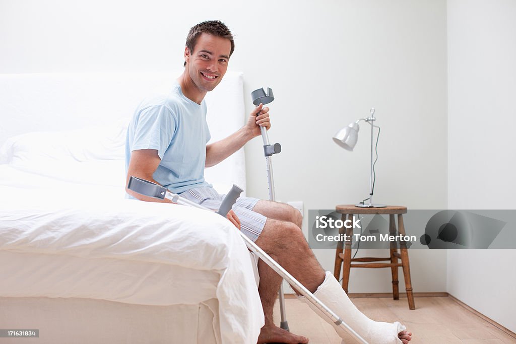 Homem com a perna quebrada sentada na cama - Royalty-free Muleta Foto de stock