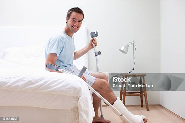 Homem Com A Perna Quebrada Sentada Na Cama - Fotografias de stock e mais imagens de Muleta - Muleta, Homens, Gesso - Equipamento Ortopédico