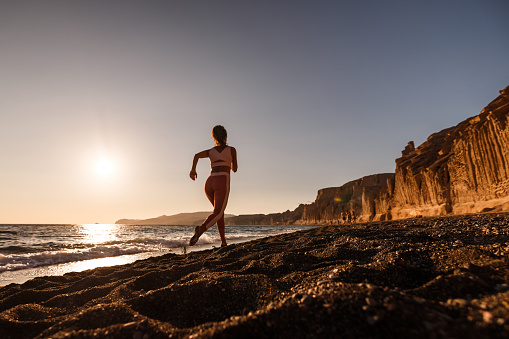 Athletic woman running on the beach during summer at sunset. Copy space.