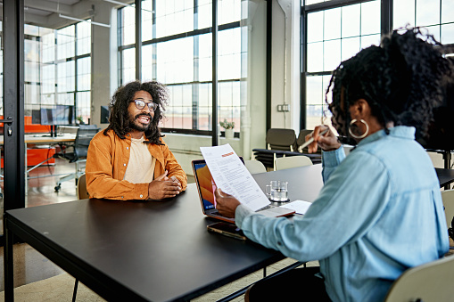 Mature Black human resources representative face to face with bearded candidate and conversing with him about his résumé.
