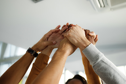 Close up of unrecognizable colleagues celebrating their success while holding their hands in unity in the office. Copy space.