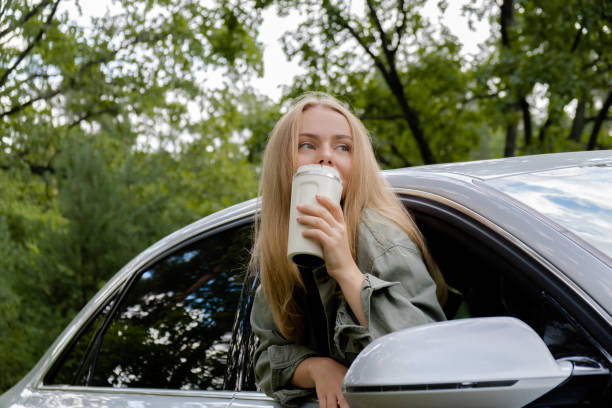istock Smiling young woman looking from car window and drinking coffee or tea from reusable thermos cup. Local solo travel on weekends concept. Exited woman explore freedom outdoors in forest. Unity with nature lifestyle, rest recharge 1716376272