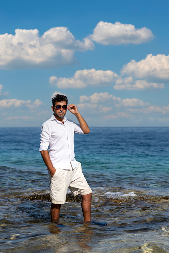 Serious man wearing white shorts and shirt poses in the sea