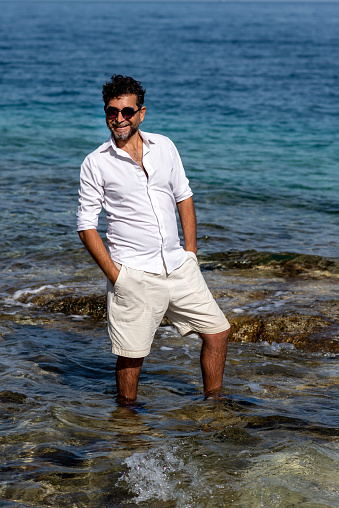 Happy man wearing white shorts and shirt poses in the sea