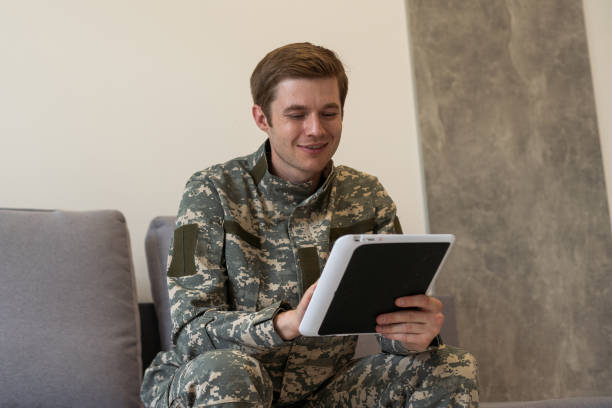 istock Smiling millennial man in camouflage uniform holding modern digital tablet, chatting with family, posing on white studio background, copy space. Modern technologies and military personnel concept. 1716407661