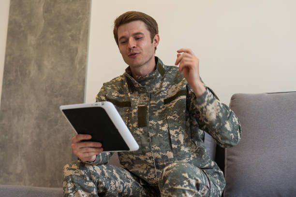 istock Smiling millennial man in camouflage uniform holding modern digital tablet, chatting with family, posing on white studio background, copy space. Modern technologies and military personnel concept. 1716411053