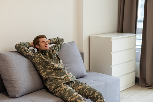 Soldier napping on soft sofa near TV in living room. Military service.