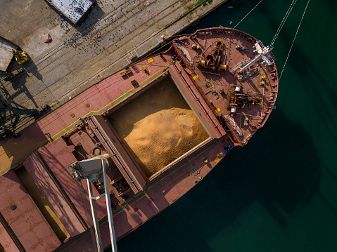 cargo ship or bulk carrier loaded to the brim with grain is preparing for departure, working sailors on deck are completing work, aerial top view