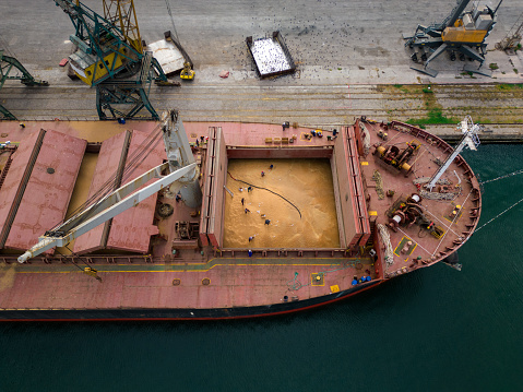 cargo ship or bulk carrier loaded to the brim with grain is preparing for departure, working sailors on deck are completing work, aerial top view