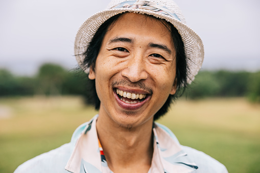 Closeup of a young smiling Japanese man wearing a hat