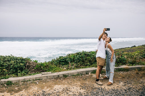 Young Japanese couple taking a selfie together with ocean view.