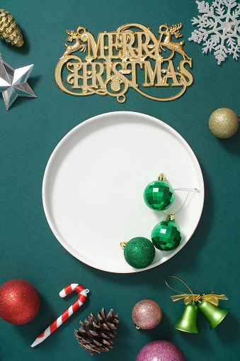 Creative background for advertising and branding product with Christmas holiday concept. Colorful decorations like baubles, bells, candy canes displayed on green background with white ceramic dish