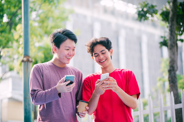 istock Happy Two Asian Man Standing On Sidewalk And Using SMartphone Together. 1716478526