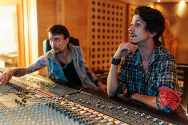 istock Two music producers siting at a mixing desk in a music studio 1716480619