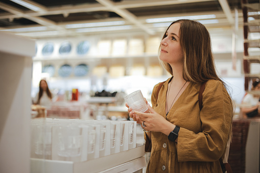 Portrait of focused young woman choosing drink glasses at store