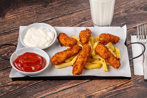 Chicken fingers and french fries with sauces on wooden table