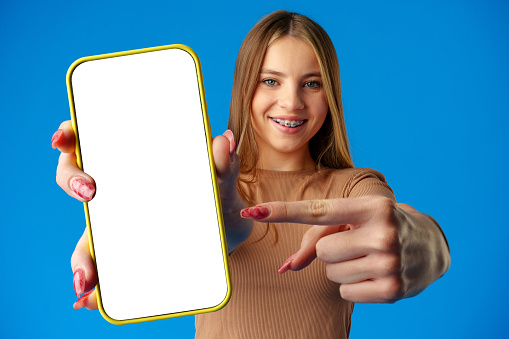Teen girl showing smartphone screen with copy space over blue background in studio