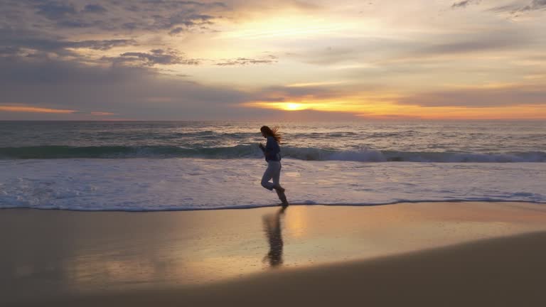 Aerial view. Beautiful woman barefoot are running In the ocean beach time evening amazing sunset, twilight