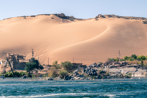Contrast between sand dunes of desert in the background and the nile river in the foreground in Egypt. Horizontal Photo