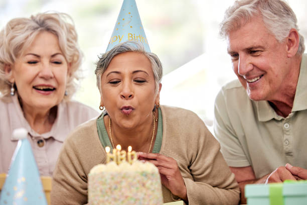 年配の女性、友人、ろうそくの誕生日ケーキ、老人ホームでのお祝いに願い、興奮。高齢者グループ、人々、そしてパーティー、イベント、引退した炎を吹くために一緒に - senior adult nursing home eating home interior ストックフォトと画像