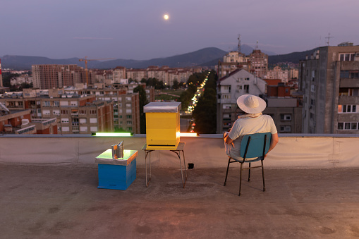 Urban beekeeper sitting by his apiary on building rooftop.