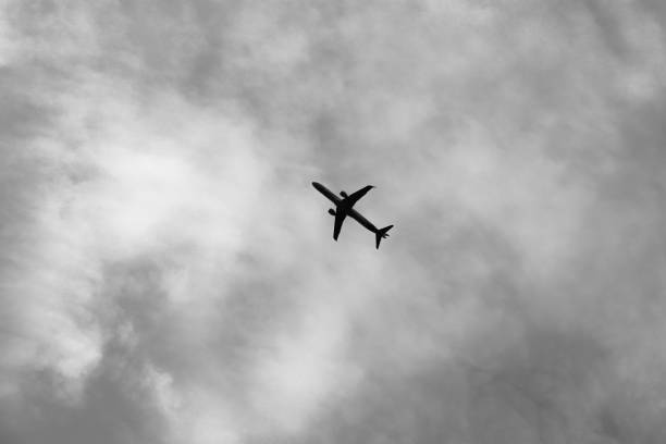istock Black and white image of a single plane flying across a cloudy sky 1716563265