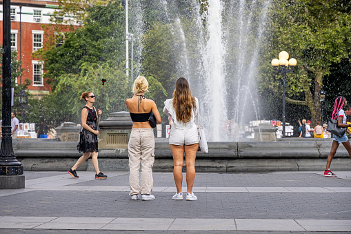 Washington Square Park, Manhattan, New York, USA - August 16th 2023:  Two young women admiring the fountain in the center of the park on a hot summer afternoon