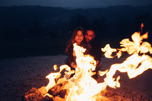 Romantic couple looking a fire near a bonfire in a mountain camping.