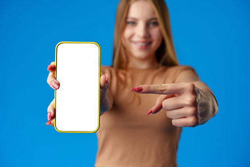 Teen girl showing smartphone screen with copy space over blue background in studio