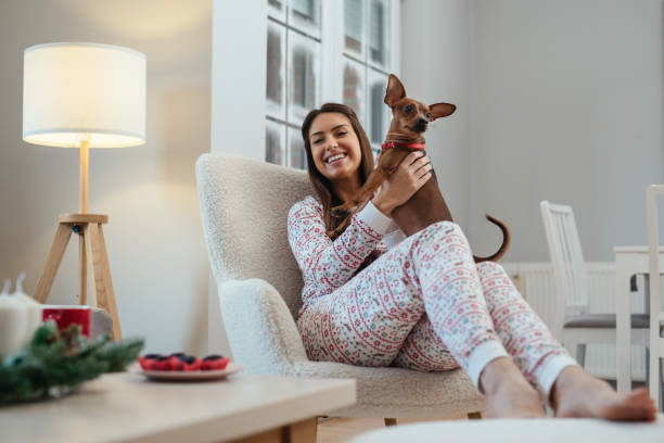 istock Girl sitting on sofa in light home interior with funny dog. 1716596541
