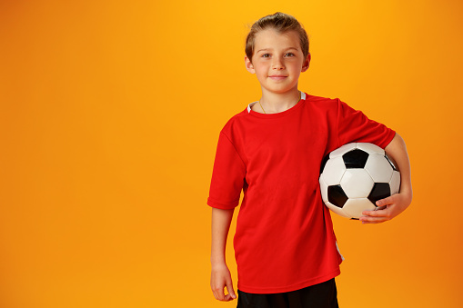 Teen boy soccer player with football ball against yellow background in studio