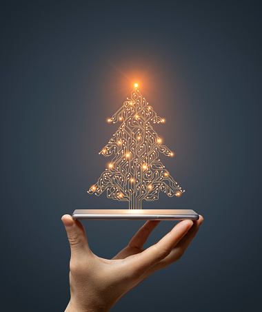 Christmas Tree concept with hand holding smartphone on dark background. This file is cleaned and retouched.